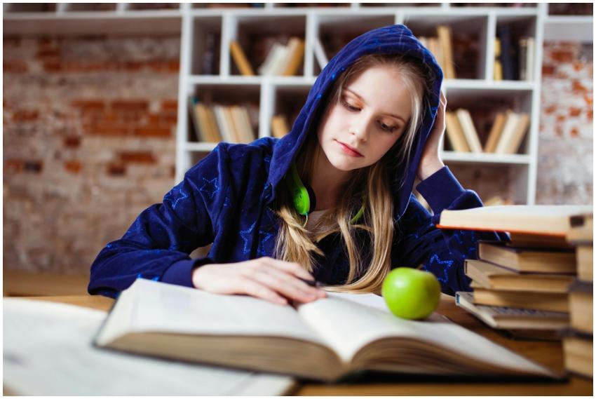 Teenage girl in blue hood reads in library, headph