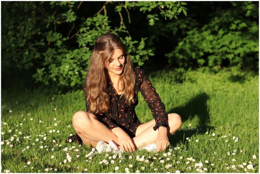 A woman in a black dress sits on grass in a sunlit