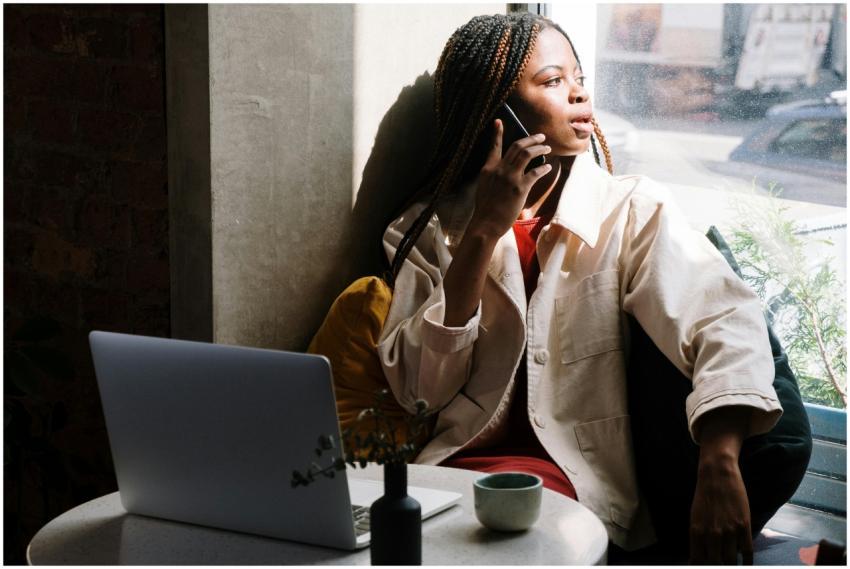 Woman with braids talking on phone in a cafe, sunl