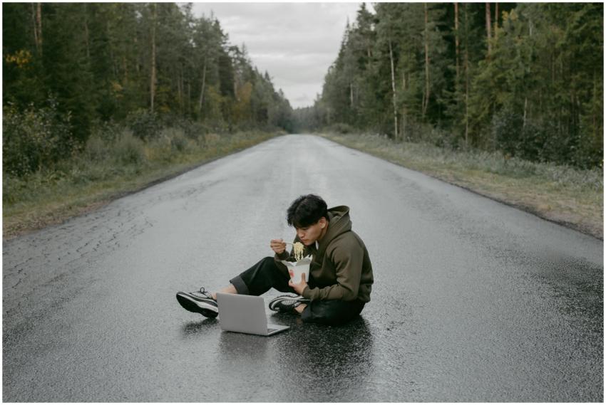 Man sitting on a deserted road eating noodles with