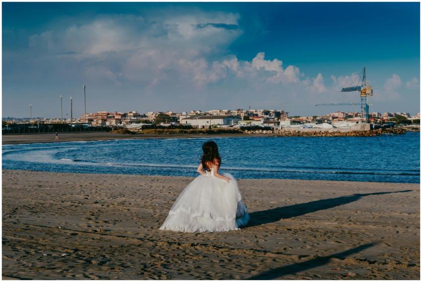 A bride in a wedding dress gazes at the serene sea