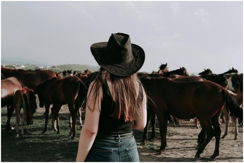 A woman in a cowboy hat observing a herd of horses