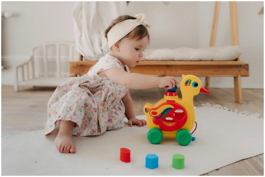 Cute baby girl in a floral dress playing with a co