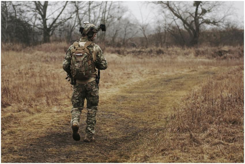 A soldier in camouflage walking along a grassy pat