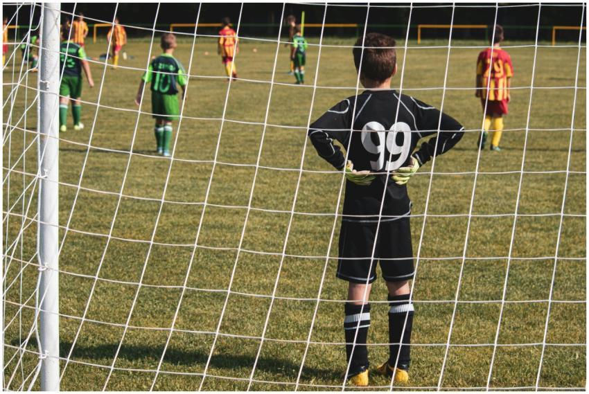 A young goalkeeper stands ready while teammates pr