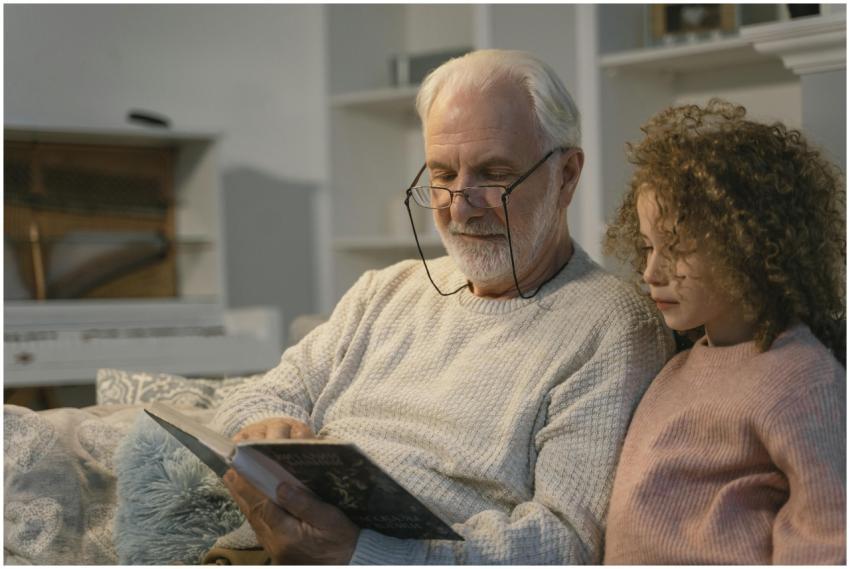 Elderly man and girl reading a book together at ho