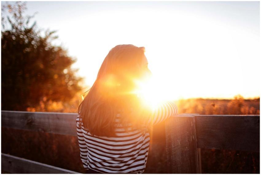 A woman leans against a wooden fence, basking in t