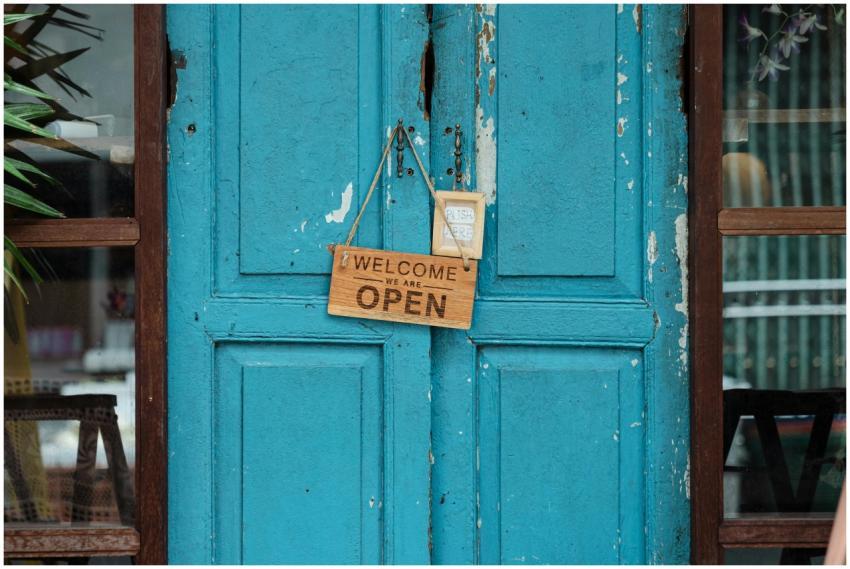 A rustic blue door with a wooden welcome sign indi