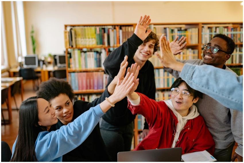 Group of happy students high-fiving in a library s