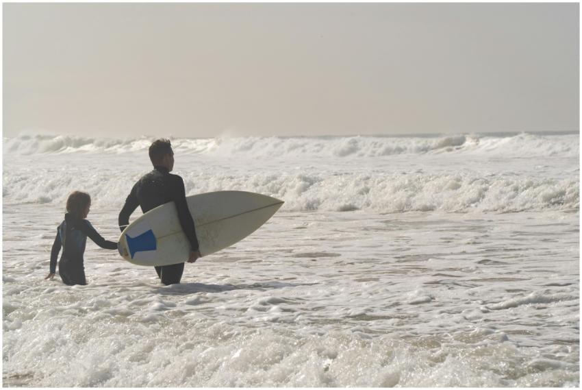 A father and child wade through ocean waves with a