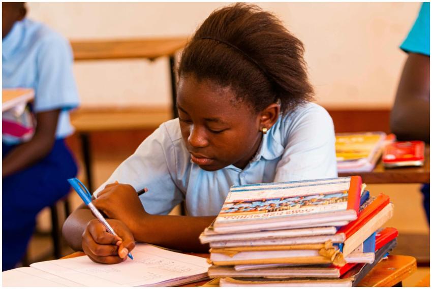 A schoolgirl in uniform writing in a notebook surr