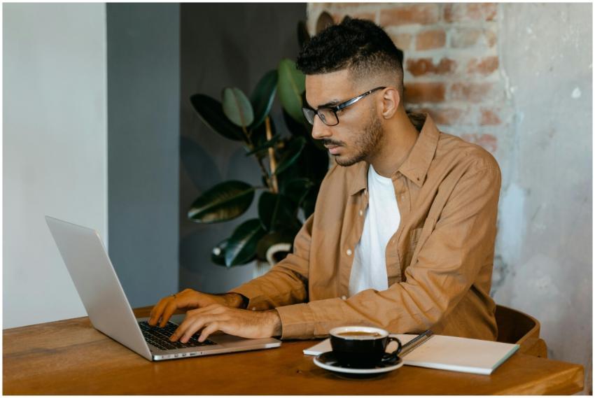 Young man with glasses working intently on laptop