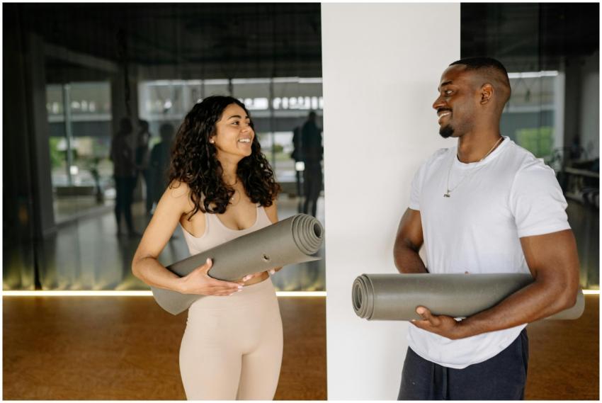 A smiling man and woman holding yoga mats, prepari