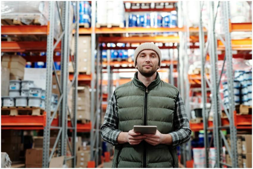 A warehouse worker wearing a beanie uses a tablet