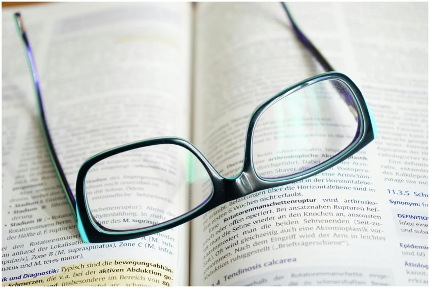 Reading glasses resting on an open textbook, symbo