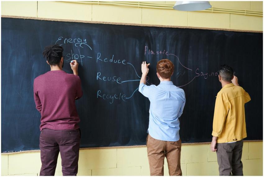 Three students writing on a chalkboard, focusing o