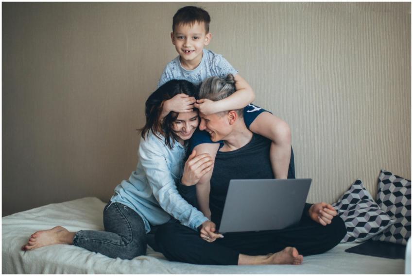 Family enjoying time together on bed, using a lapt