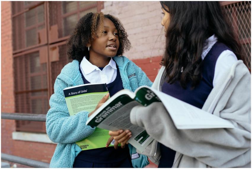 Two schoolgirls discussing lessons outdoors, holdi