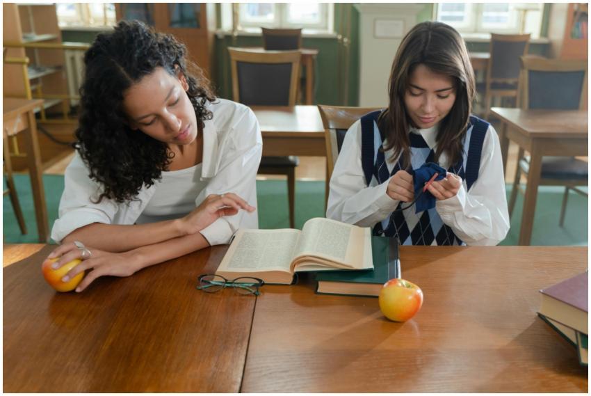 Two women study together in a library, surrounded