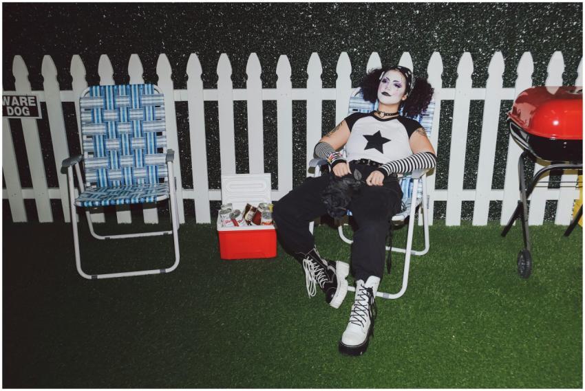 A person in gothic attire relaxes outdoors near a