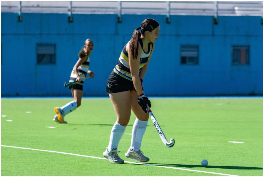 Two female field hockey players in action on an ou