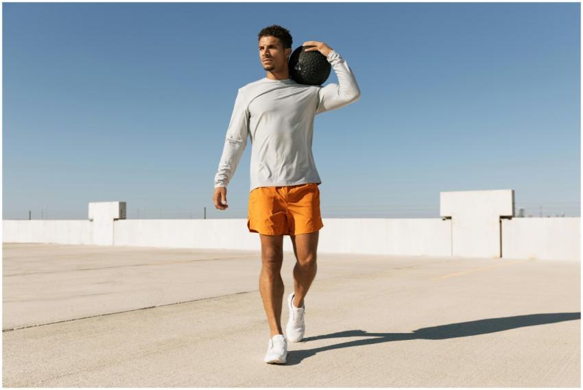 Man in orange shorts exercises with a medicine bal