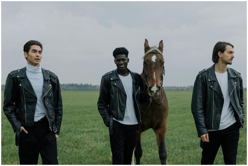 Three men in leather jackets walk in a grassy fiel