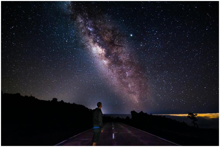 A lone figure gazes at the star-filled sky with th