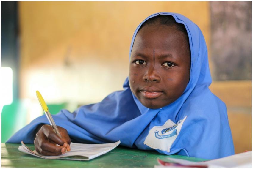 Young girl in blue hijab writing at desk in classr
