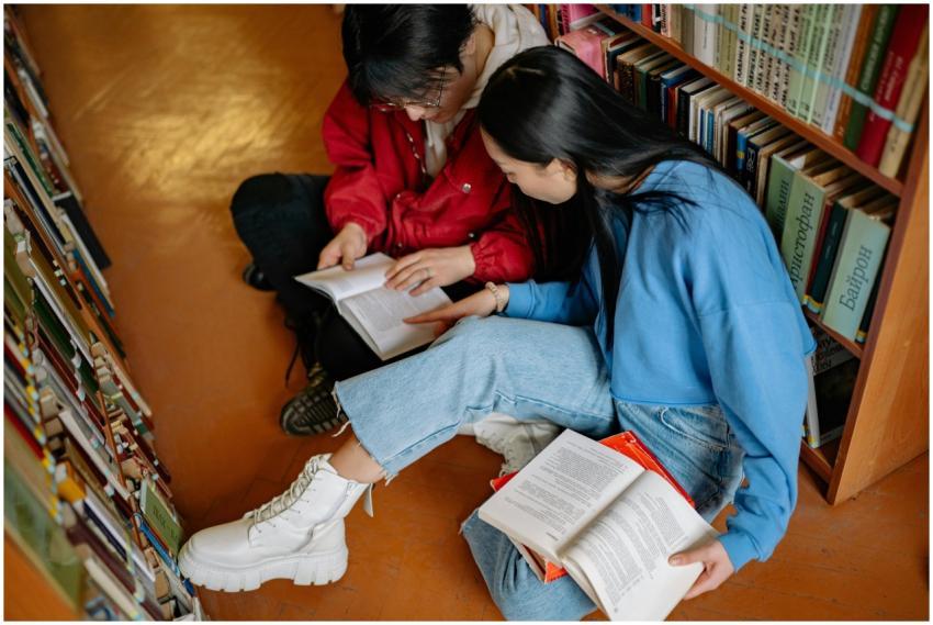 Two students sitting and reading books in a librar