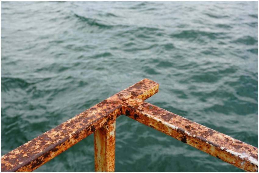 Close-up of a rusted metal railing with ocean wave