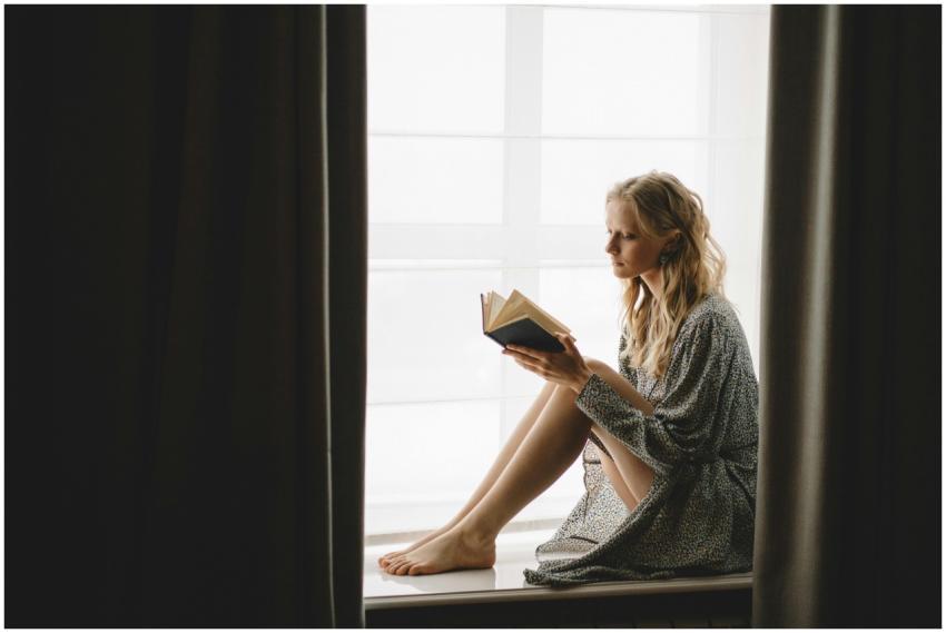 A young woman reading a book by the window with so