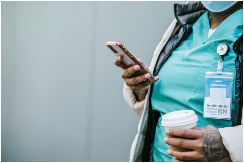Nurse in scrubs checking phone while holding a tak