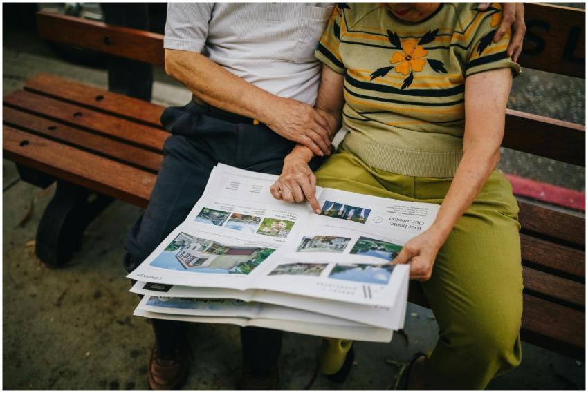 Elderly couple sitting outdoors, reading and embra