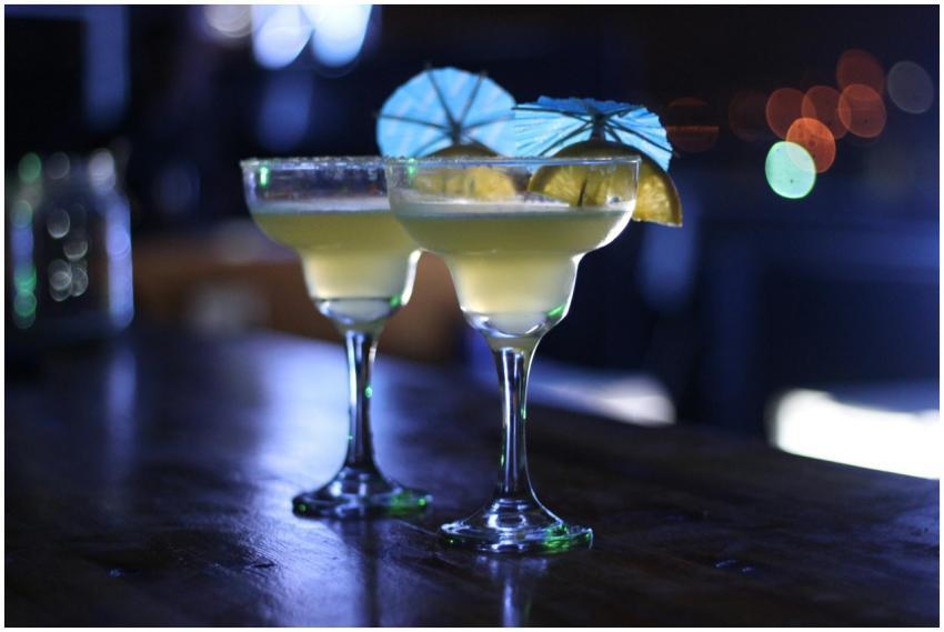 Two cocktails with lime and umbrellas on a dimly l