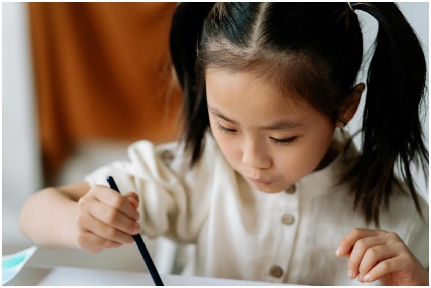 A young Asian child intently painting in an art wo