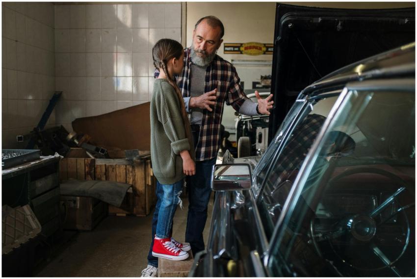 Father teaching daughter about cars in a workshop,