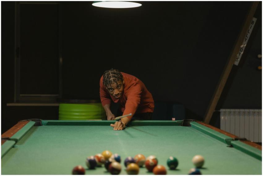 A person skillfully aiming a pool cue on a billiar