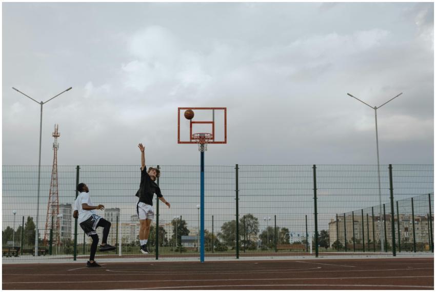 Two men playing basketball outdoors, jumping for a