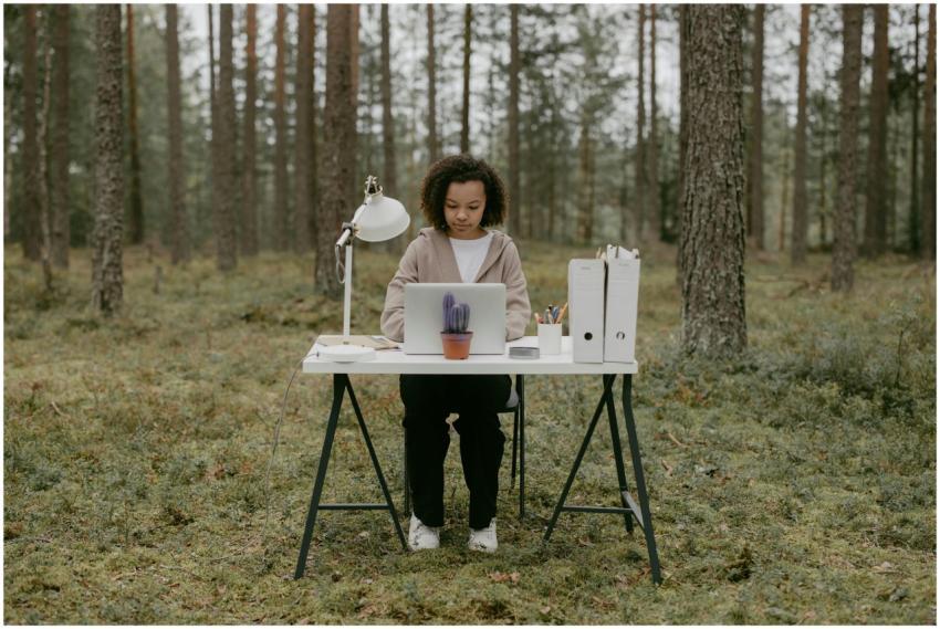 A woman sits at a desk in a forest, working remote