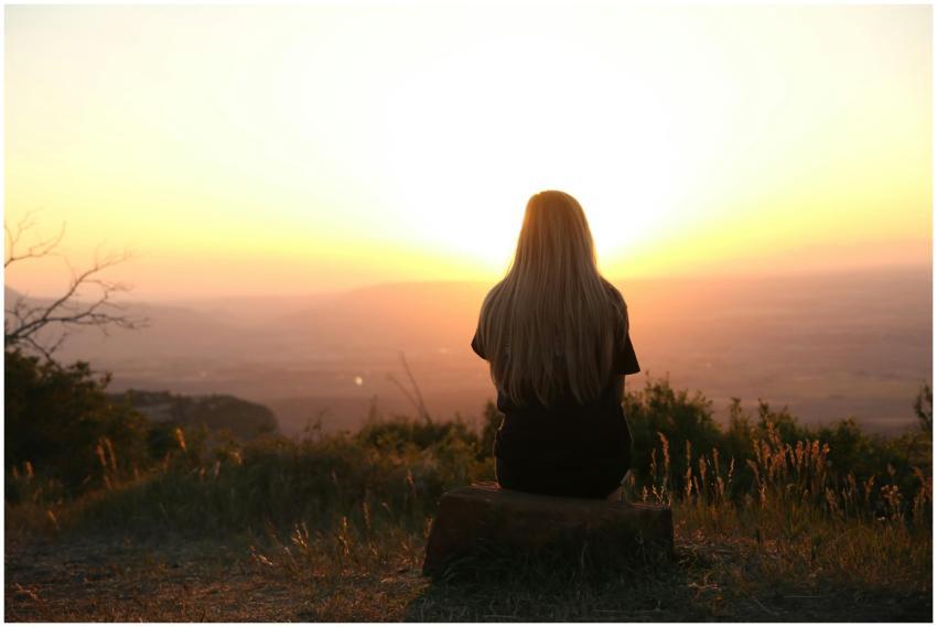 Woman sitting in nature, watching sunset over fiel