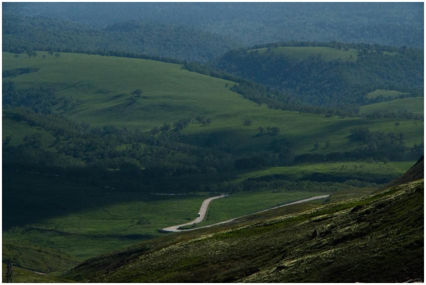 A winding road through a lush green valley surroun
