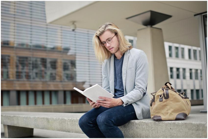 A young adult man reading a book outdoors on a uni