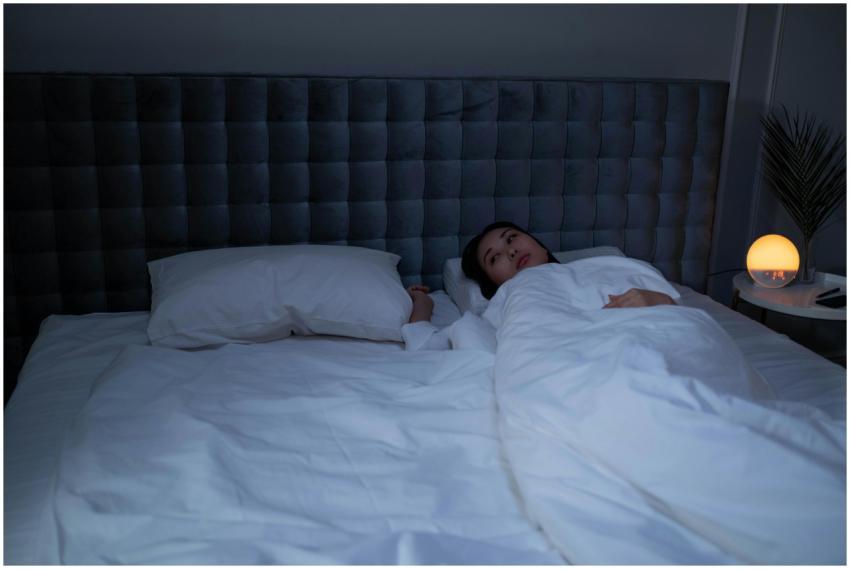 An Asian woman lying awake under soft white beddin