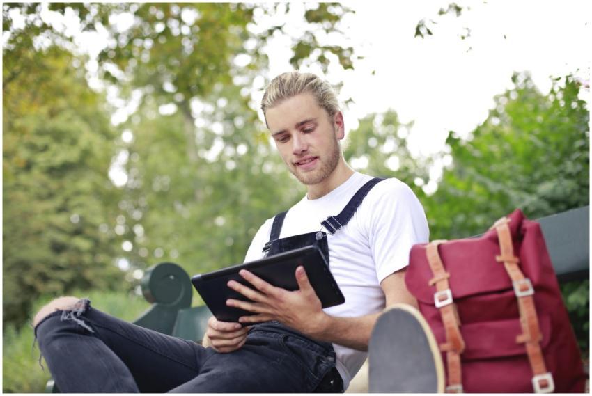 Casual young man sitting on a park bench using a t
