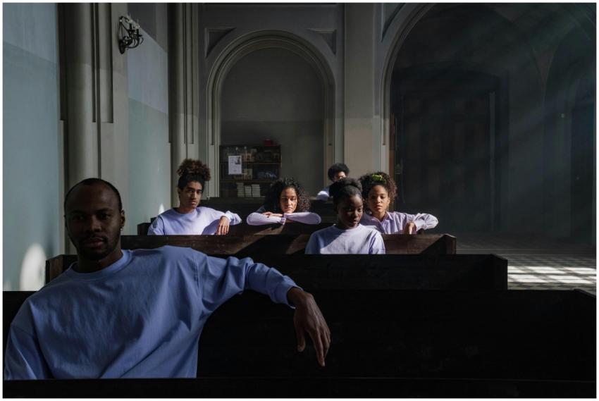 A thoughtful group sits in church pews, light stre