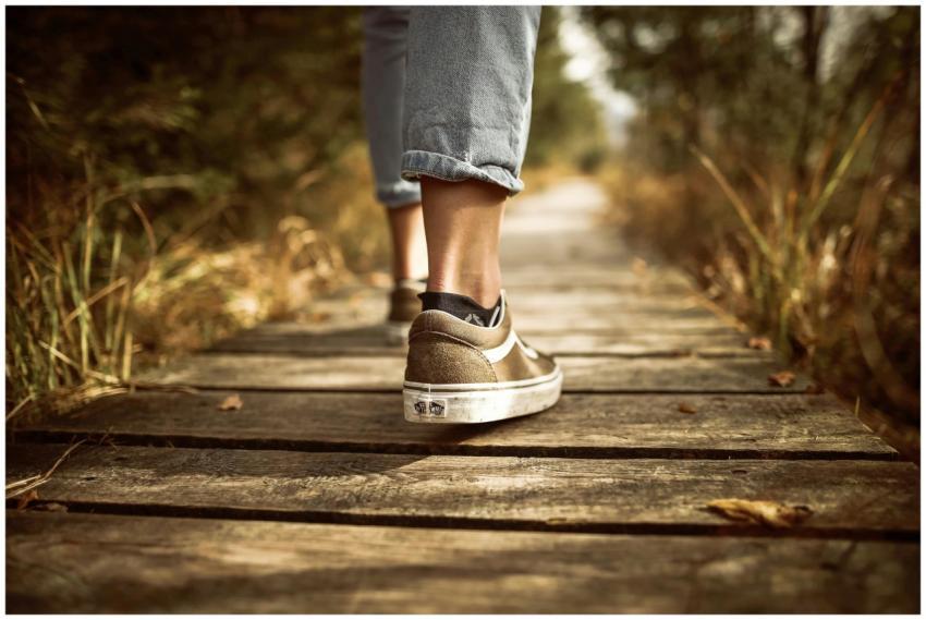 Person wearing sneakers walking on a wooden path i