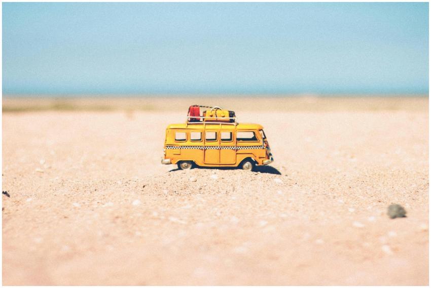 A toy van on a sandy beach evokes summer travel an