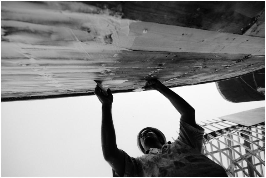 A fisherman works meticulously repairing a boat bo
