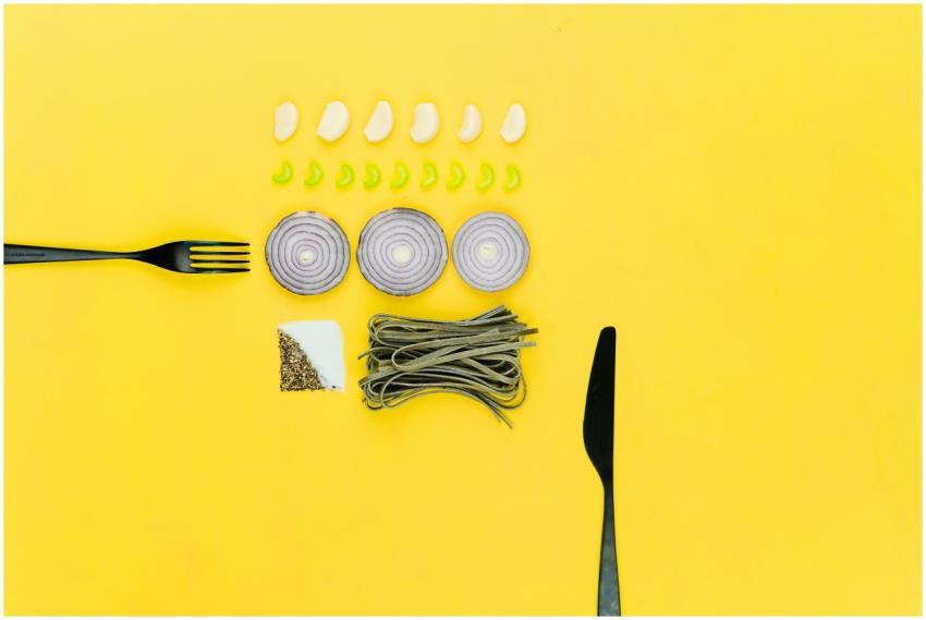 A colorful flatlay of pasta, onion, garlic, herbs,